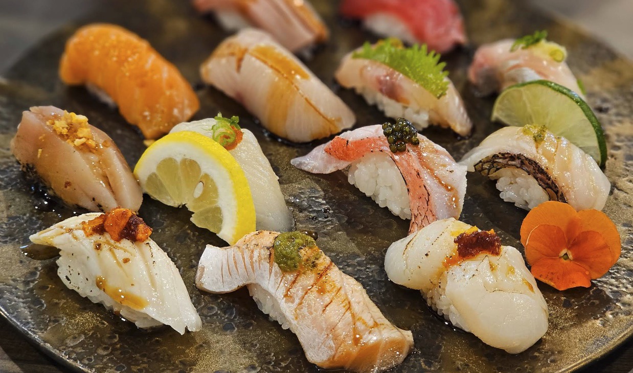 The twelve-piece chef's choice: assorted nigiri on a dark ceramic platter, several pieces torched, sauced, or garnished.