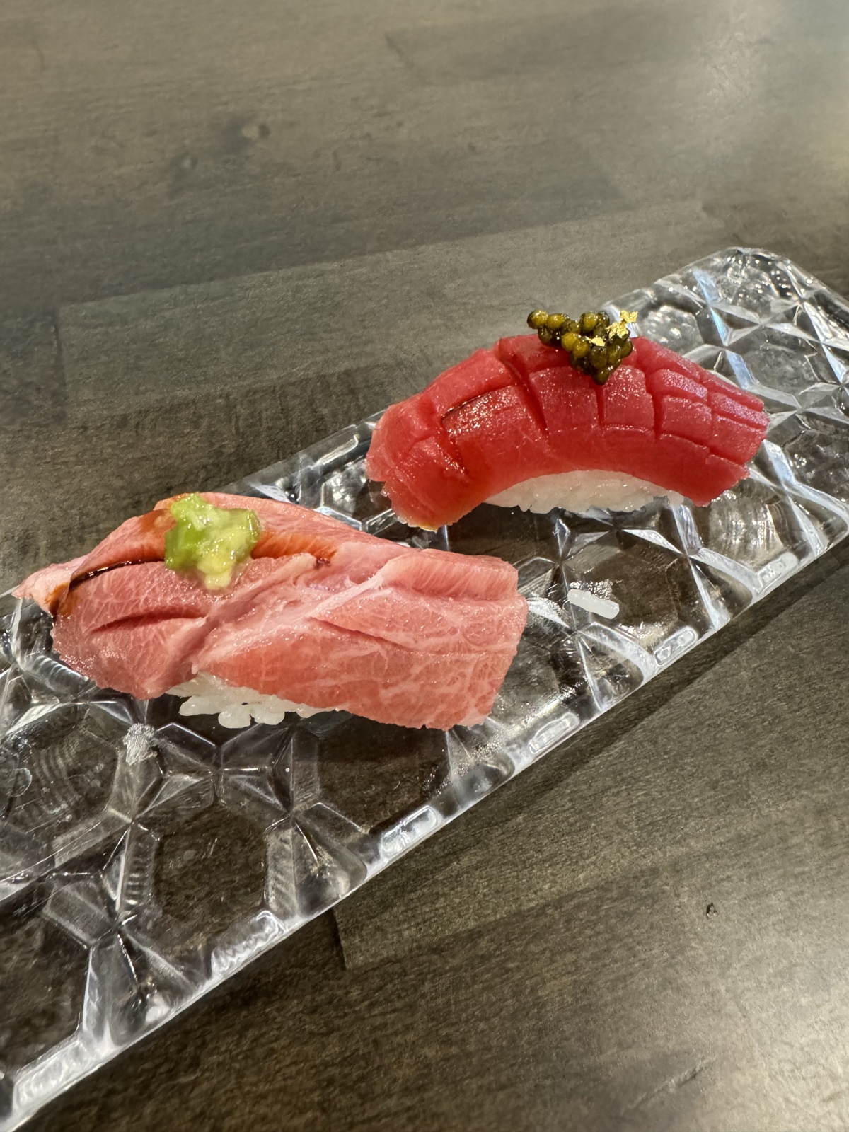 Two tuna nigiri on a crystal glass tray: fatty otoro with wasabi, lean akami topped with caviar and gold leaf.